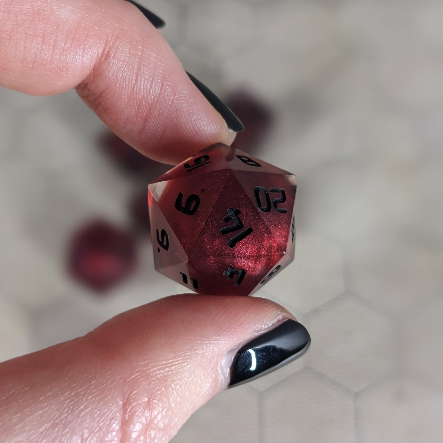 The d20 die is being held up to the camera to show off the red, spherical insert and the dark glow the black numbers give in the clear shell. The 14 face is most angled toward the camera.
