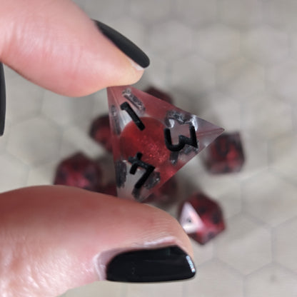The d4 die is being held up to the camera to show off the red, spherical insert and the dark glow the black numbers give in the clear shell. The face with 1, 3, and 4 in the corners is angled toward the camera.
