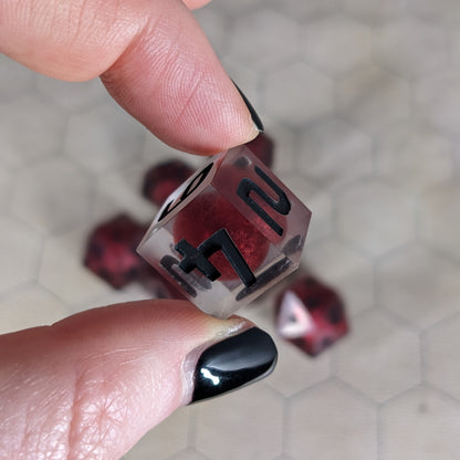 The d6 die is being held up to the camera to show off the red, spherical insert and the dark glow the black numbers give in the clear shell. The 4 and 2 faces are angled toward the camera.