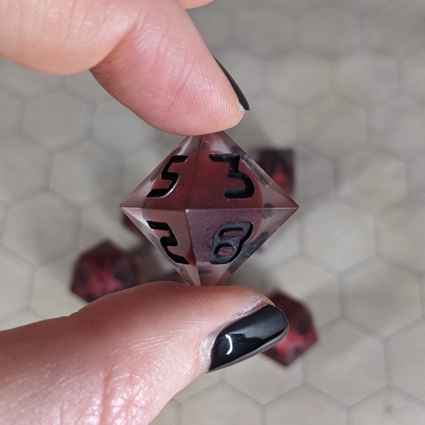 The d8 die is being held up to the camera to show off the red, spherical insert and the dark glow the black numbers give in the clear shell. The 5, 3, 2, and 8 faces are angled toward the camera.