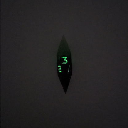 A high angle view of a diamond d3 with swirls of black and green with purple numbers that glow in the dark on a white background. This photo is taken in the dark to show the purple numbers glowing green in the dark.