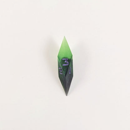 A high angle view of a diamond d3 with swirls of black and green with purple numbers that glow in the dark on a white background.