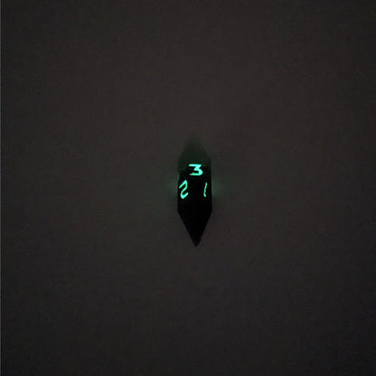 A mid angle view of a diamond d3 with swirls of black and green with purple numbers that glow in the dark on a white background. This photo was taken in the dark to show the purple numbers glowing green in the dark.