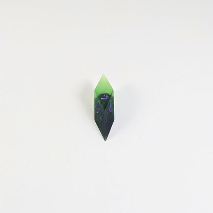 A mid angle view of a diamond d3 with swirls of black and green with purple numbers that glow in the dark on a white background.