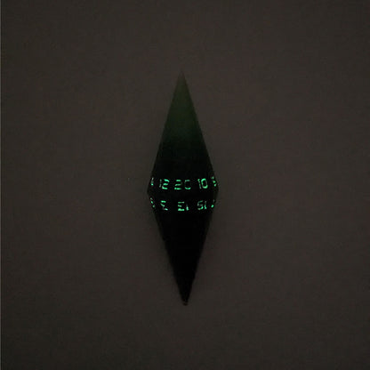 A high angle view of a diamond d20 with swirls of black and green with purple numbers that glow in the dark on a white background. This photo is taken in the dark to show the purple numbers glowing green in the dark.