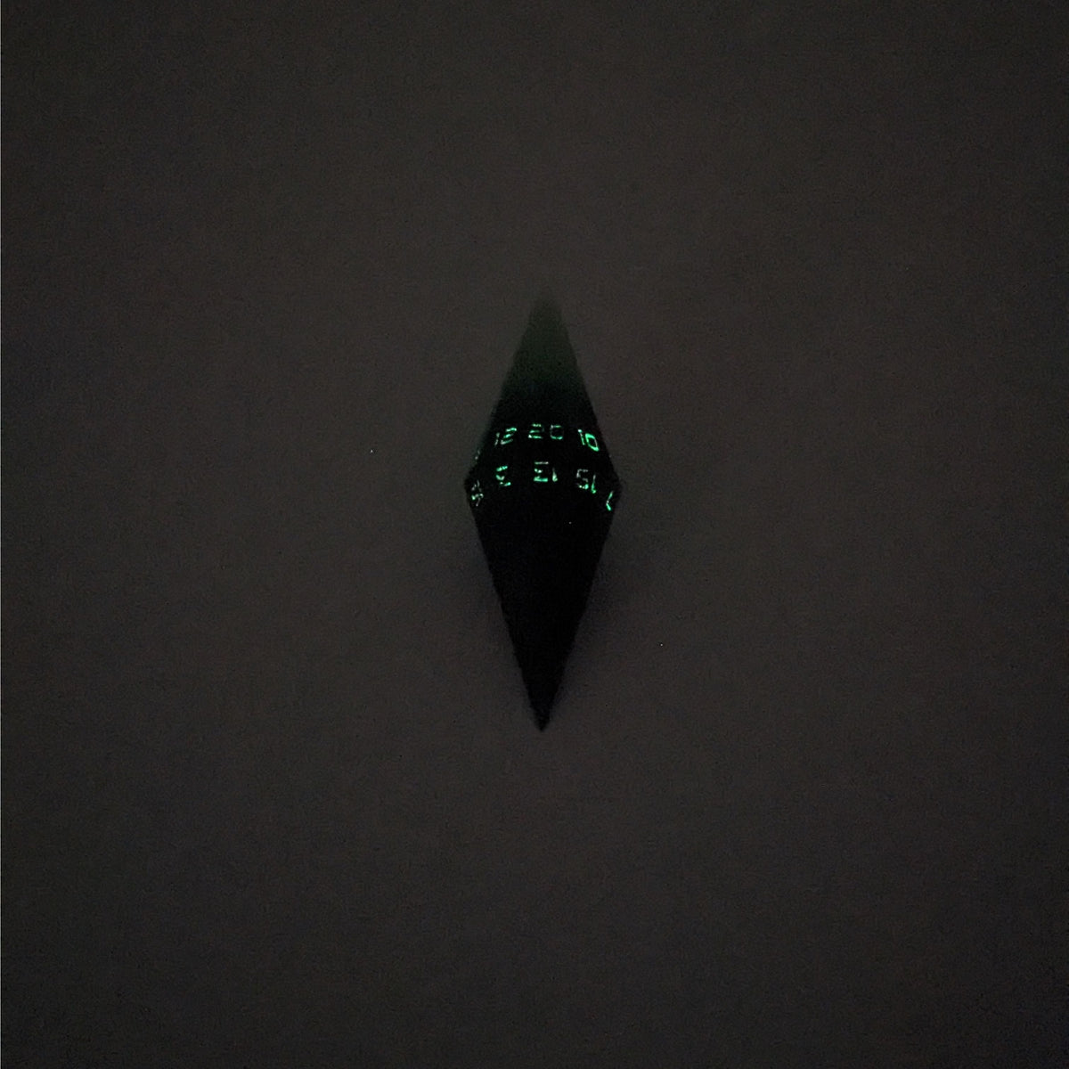 A mid angle view of a diamond d20 with swirls of black and green with purple numbers that glow in the dark on a white background. The photo is taken in the dark to show the purple numbers glowing green in the dark.