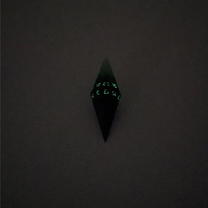 A mid angle view of a diamond d20 with swirls of black and green with purple numbers that glow in the dark on a white background. The photo is taken in the dark to show the purple numbers glowing green in the dark.