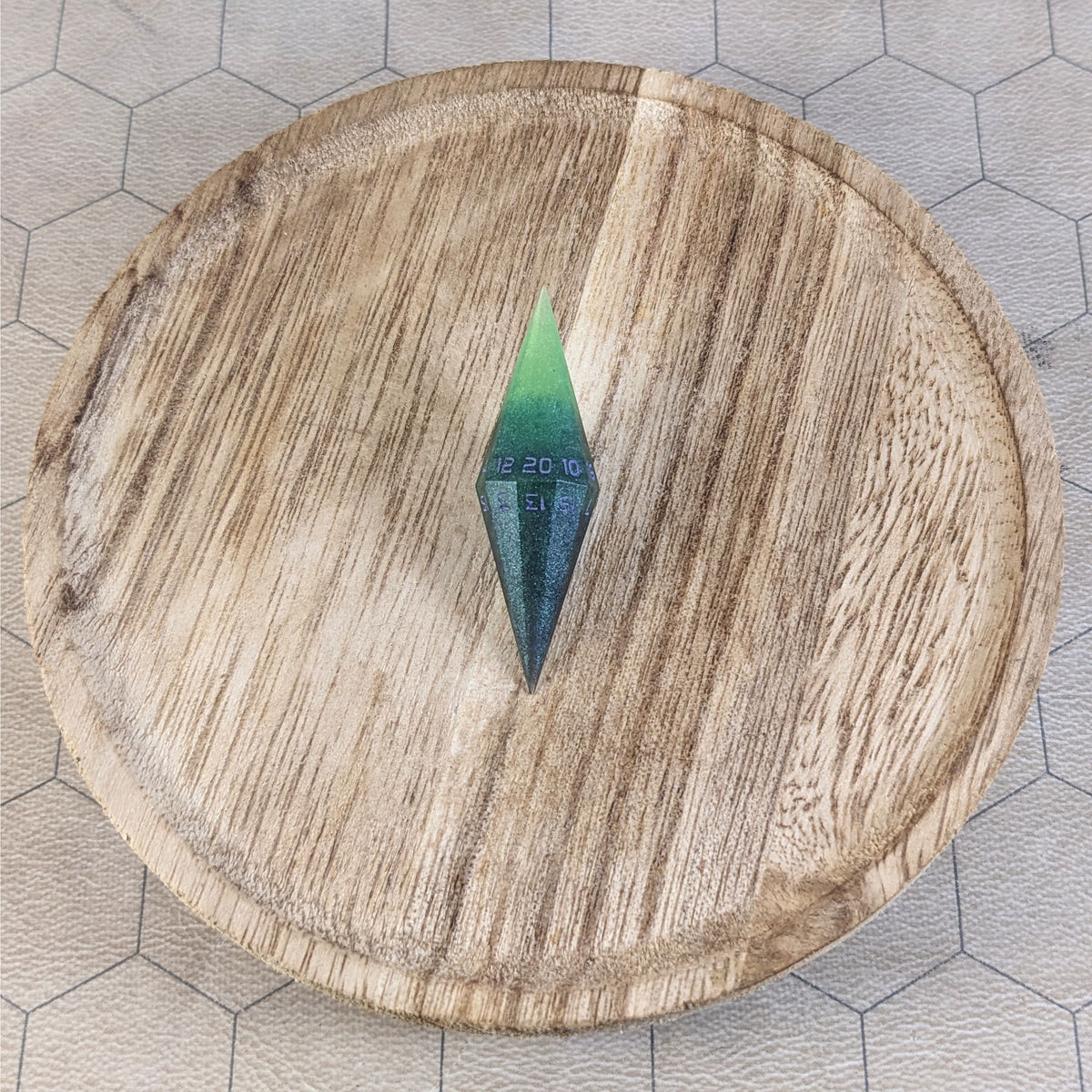A high angle view of a diamond d20 with swirls of black and green with purple numbers that glow in the dark. It is sitting in the center of a wooden circle.