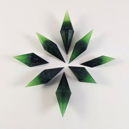 A complete set of diamond shaped resin dice featuring 2 d20s. These handmade dice are black and green with purple numbers that glow in the dark and are clustered in a circle with the bottom points angled toward a central point on a white background.