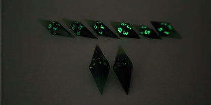 A straight on photo of a diamond set of DnD dice that are black and green with purple numbers that glow in the dark focusing on 2 d20s in the center. The d20 on the left has the 1 face up and the d20 on the right has the 20 face up. The other 6 dice are lined up in the background but are out of focus, while the d20s are in sharp focus. The photo is taken in the dark to show the purple numbers glowing green.