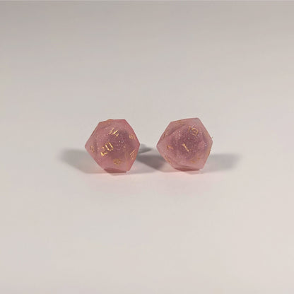 A single pair of the larger size handmade d20 earrings with titanium hardware that are medium pink with gold numbers on a white background. The earring on the left centers the 20 face and the earring on the right centers the 1 face.
