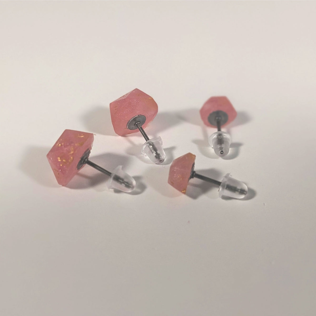 Two pairs of handmade d20 earrings that are medium pink with gold numbers turned to show the titanium hardware and bell shaped rubber backs.