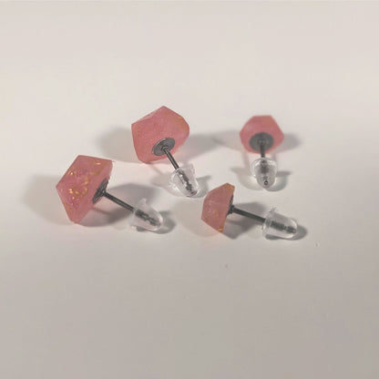 Two pairs of handmade d20 earrings that are medium pink with gold numbers turned to show the titanium hardware and bell shaped rubber backs.