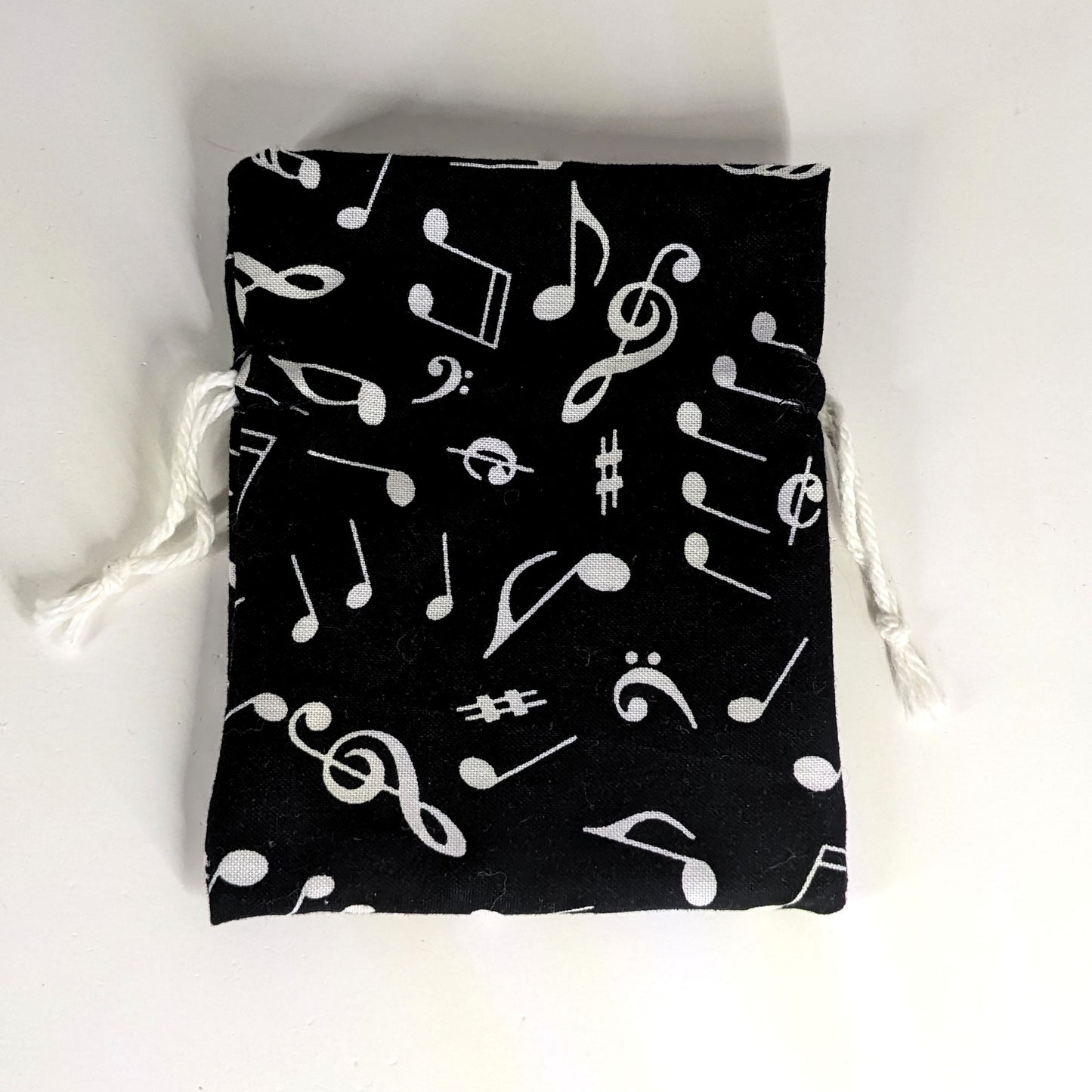 A small, handmade dice bag that is black with a white music notation pattern lays flat on a white background.