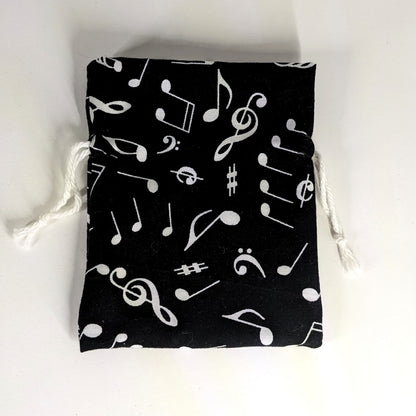 A small, handmade dice bag that is black with a white music notation pattern lays flat on a white background.