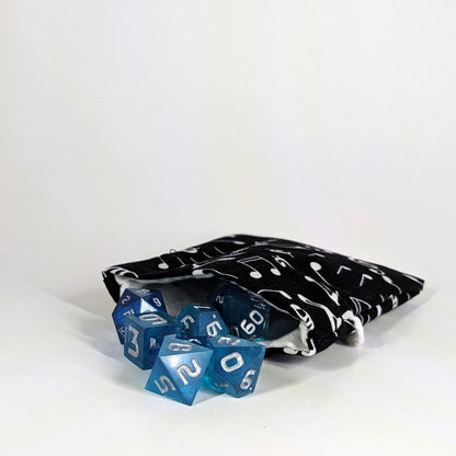 A small, handmade dice bag that is black with a white music notation pattern lays open with a set of blue, dnd dice spilling out of it on a white background.