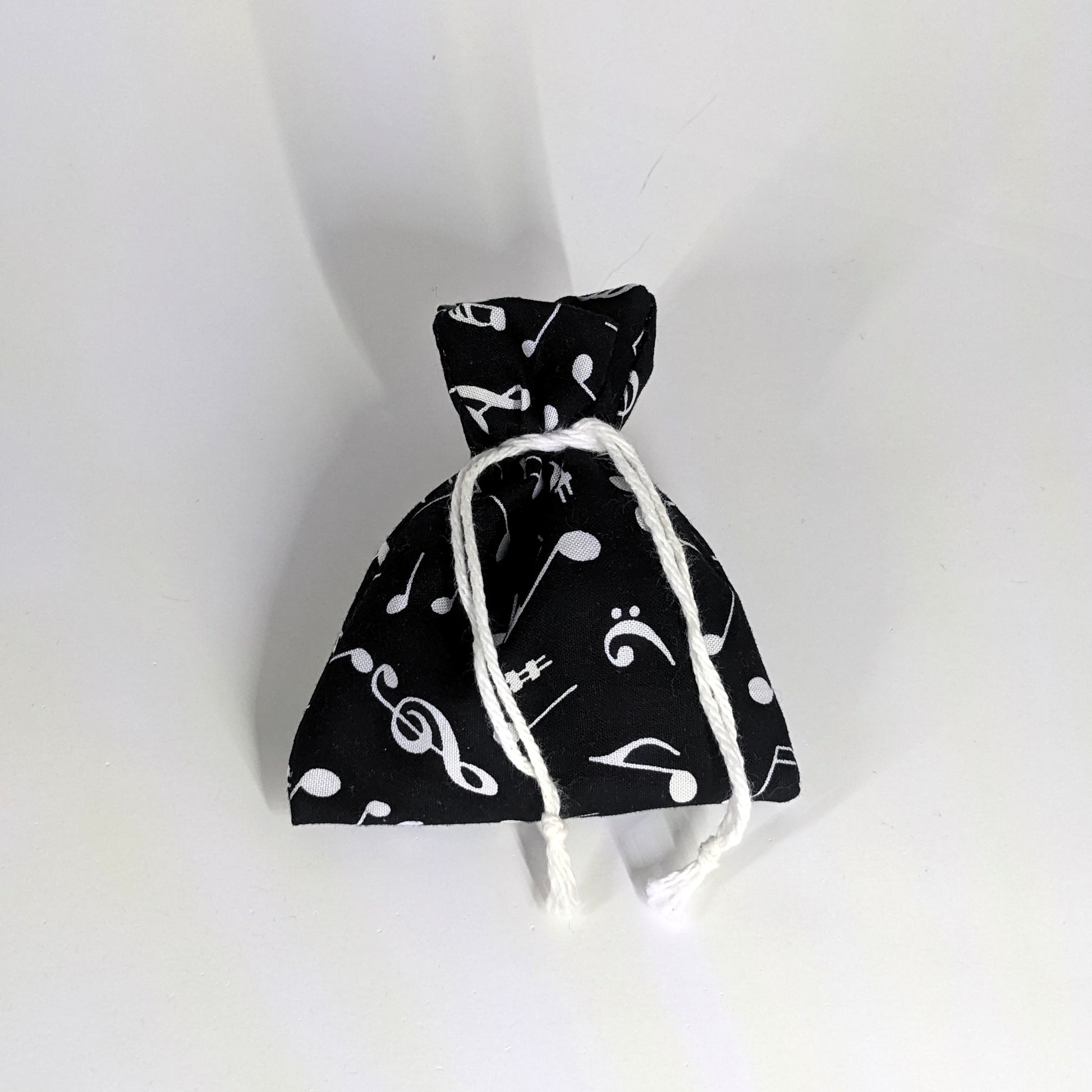A small, handmade dice bag that is black with a white music notation pattern is tied closed on a white background.
