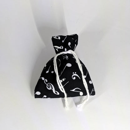 A small, handmade dice bag that is black with a white music notation pattern is tied closed on a white background.