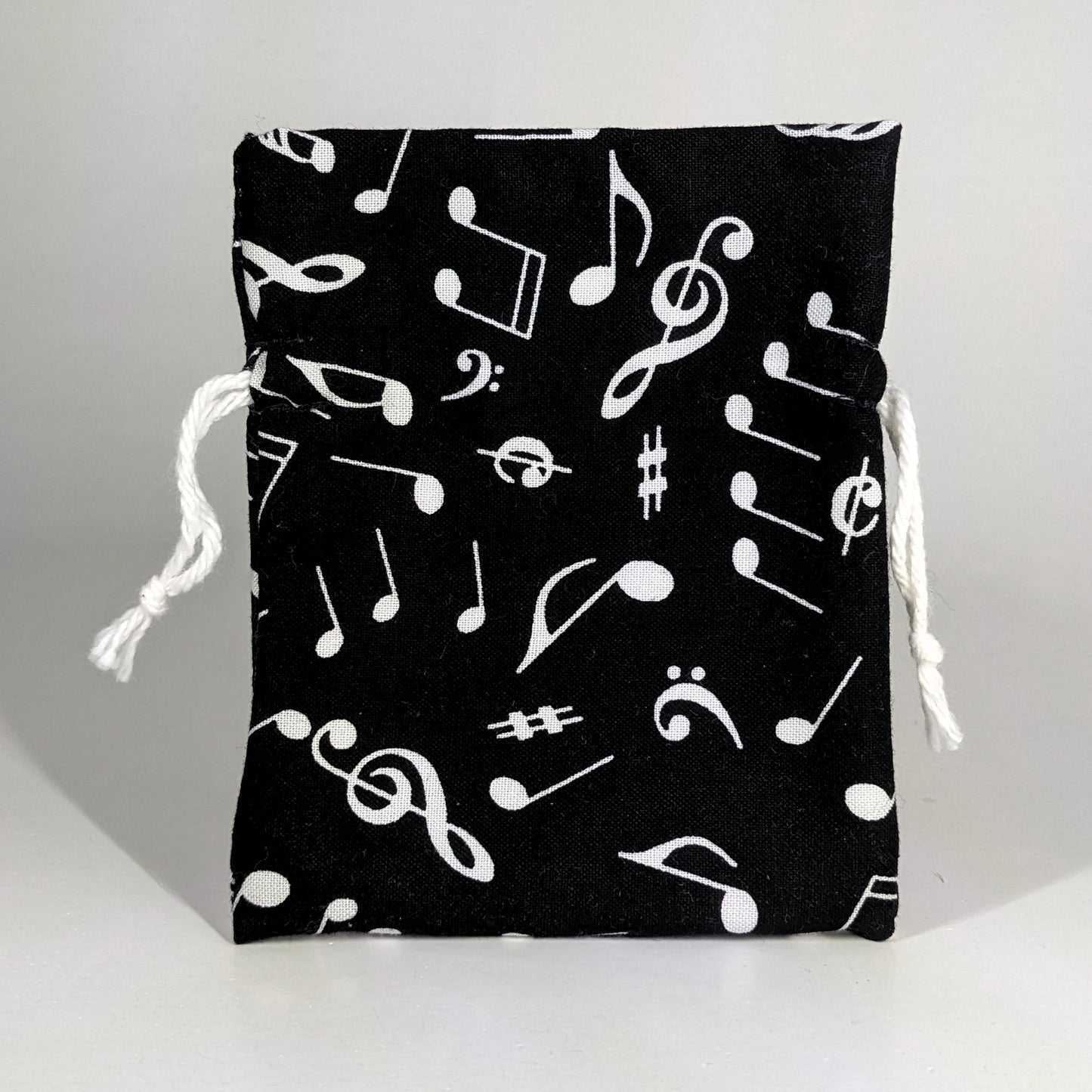 A small, handmade dice bag that is black with a white music notation pattern stands upright on a white background.