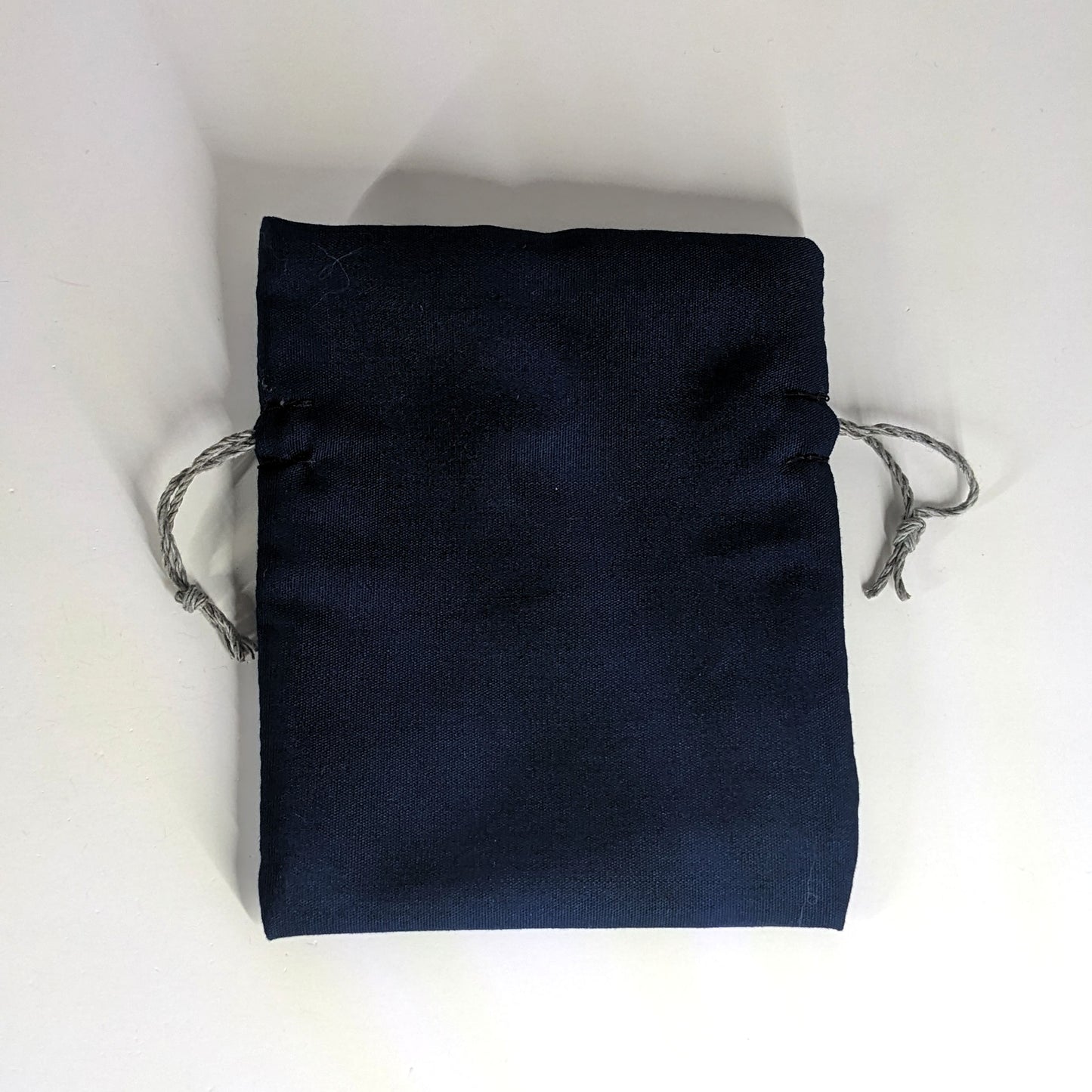 A small, handmade dice bag that is navy lays flat on a white background.