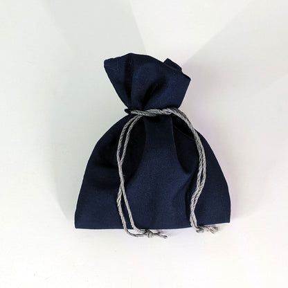 A small, handmade dice bag that is navy is tied closed on a white background.
