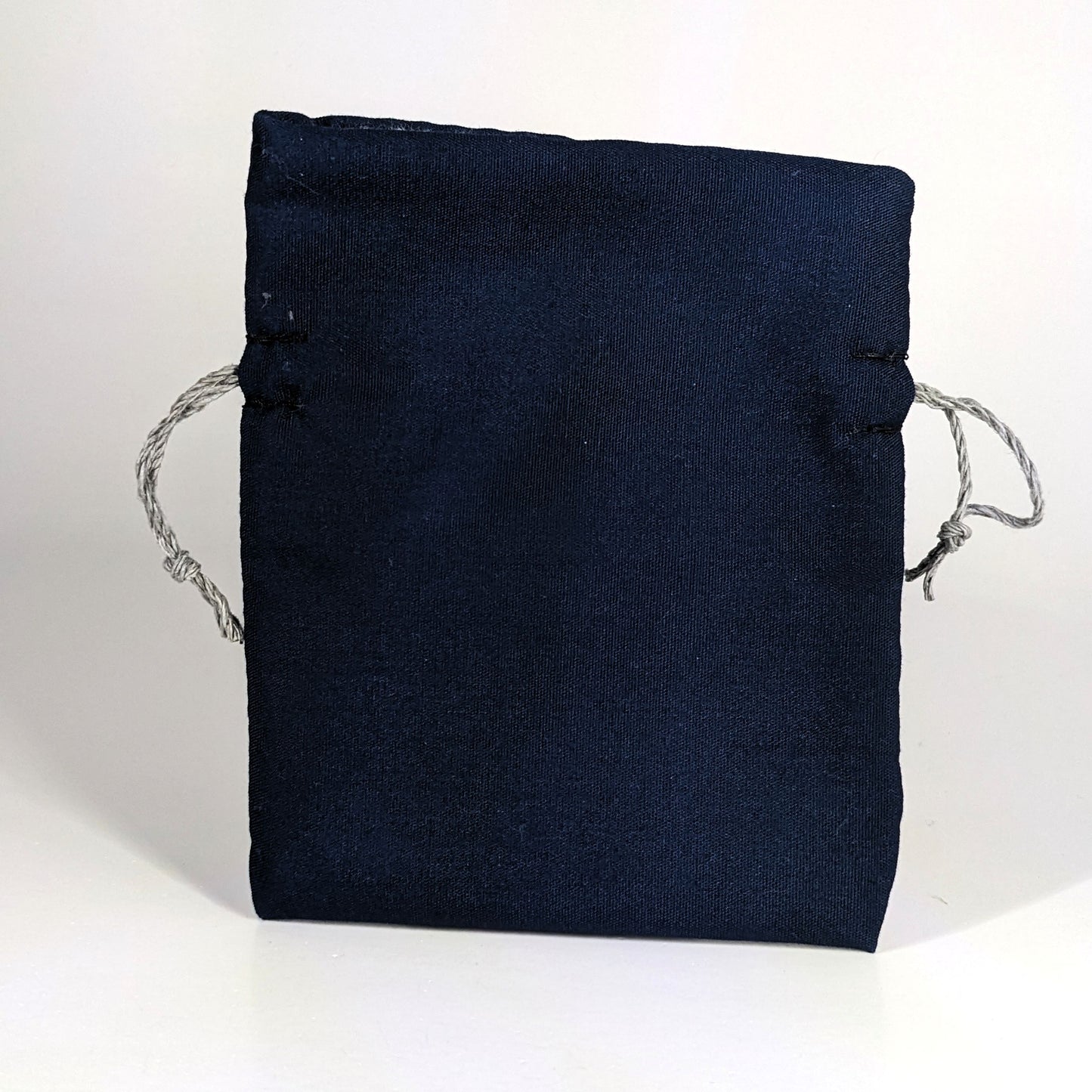 A small, handmade dice bag that is navy stands upright on a white background.