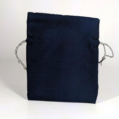 A small, handmade dice bag that is navy stands upright on a white background.