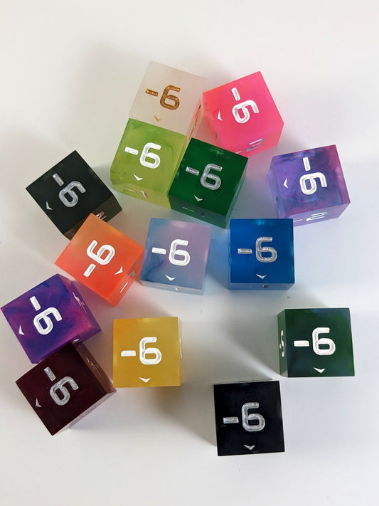 A collection of negative spindown d6s of a variety of colors on a white background. Each die has the -6 face up.