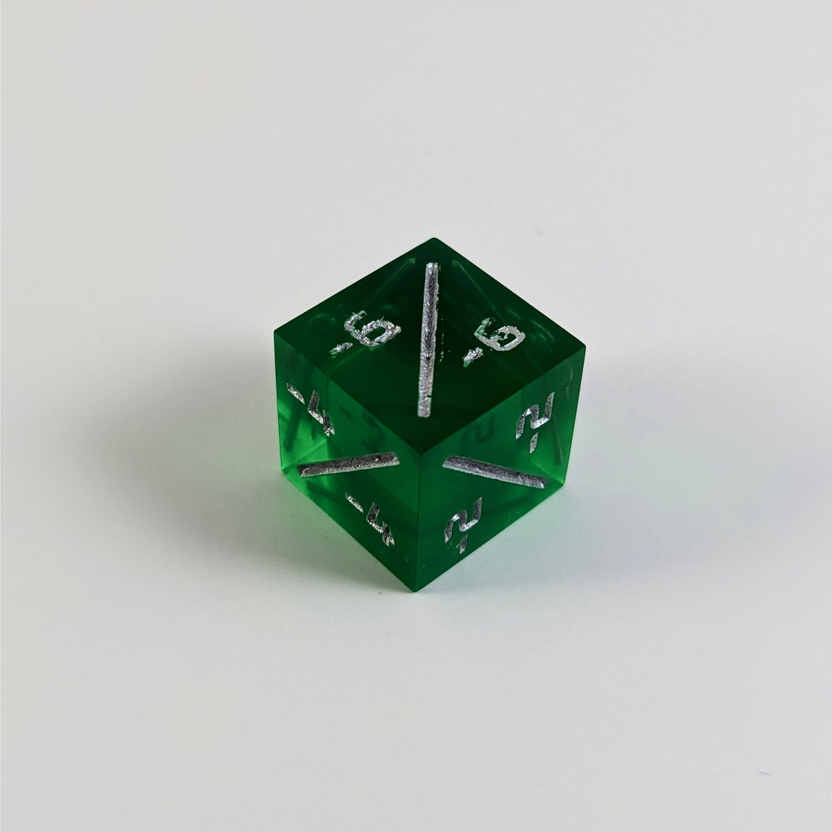 A mid angle photo of a green negative counter d6 with silver numbers sits on a white background with the corner of the -6/-6, -4/-4, and -2/-2 faces angled toward the camera.