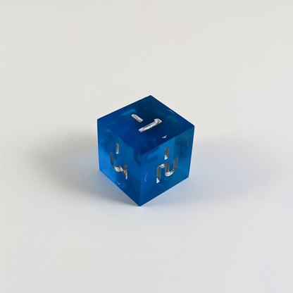 A mid angle photo of a blue negative spindown d6 with silver numbers sits on a white background with the corner of the -1, -2, and -3 faces angled toward the camera.