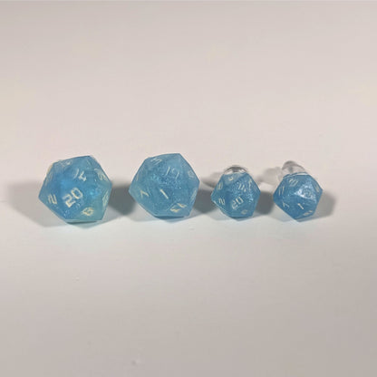 Two pairs of handmade d20 earrings with titanium hardware that are oceanic shades of blue and green with sandy white numbers on a white background sit in a line with the larger pair on the left and the smaller pair on the right. The earrings on the left of each pair centers the 20 face and the earrings on the right of each pair centers the 1 face.