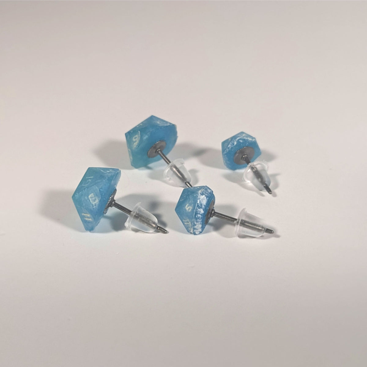 Two pairs of handmade d20 earrings that are oceanic shades of blue and green with sandy white numbers turned to show the titanium hardware and bell shaped rubber backs.