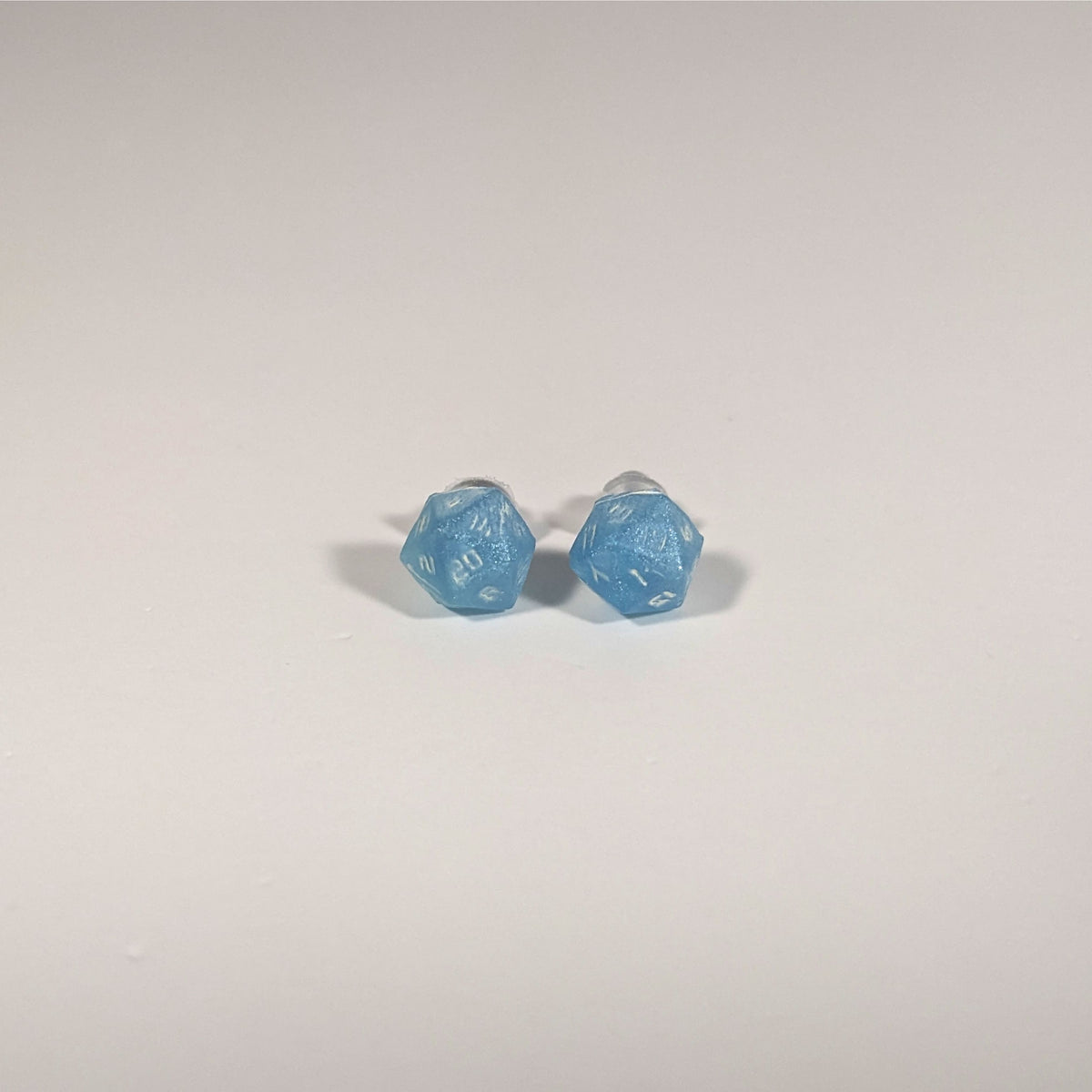 A single pair of the smaller size handmade d20 earrings with titanium hardware that are oceanic shades of blue and green with sandy white numbers on a white background. The earring on the left centers the 20 face and the earring on the right centers the 1 face.
