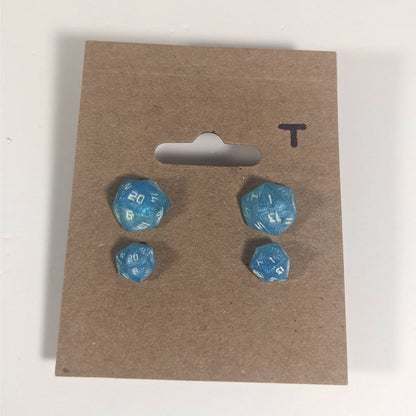 Two pairs of handmade d20 earrings with titanium hardware that are oceanic shades of blue and green with sandy white numbers on a kraft brown earring card with a T in the top right corner. The earrings on the left of each pair centers the 20 face and the earrings on the right of each pair centers the 1 face.