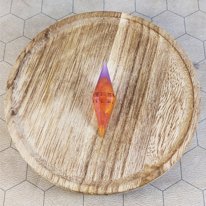 An orange and purple diamond d20 with black numbers sits in the center of a wooden circle on a beige hex map.