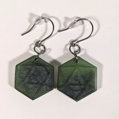 A pair of dark green and dark silver dangly, flat d20 earrings with silver color titanium and niobium hardware and bell shaped rubber backs on a white background. The earring on the left has a 20 on it and the earring on the right has a 1 on it, both in a sci-fi style font.
