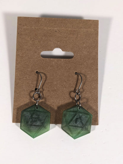 A pair of dark green and dark silver dangly, flat d20 earrings with silver color titanium and niobium hardware on a kraft earring card on a white background. The earring on the left has a 20 on it and the earring on the right has a 1 on it, both in a fantasy style font.