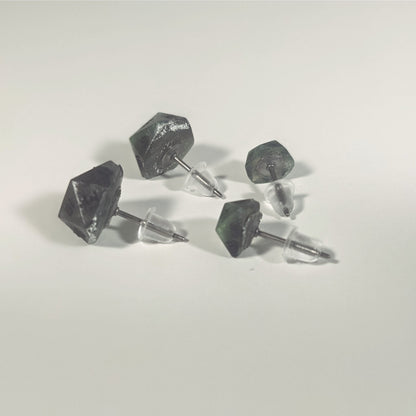 Two pairs of handmade d20 earrings that are green and dark silver with black numbers turned to show the titanium hardware and bell shaped rubber backs.