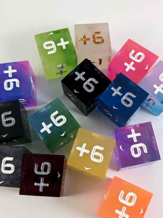 A collection of positive spindown d6s of a variety of colors on a white background. Each die has the +6 face up.