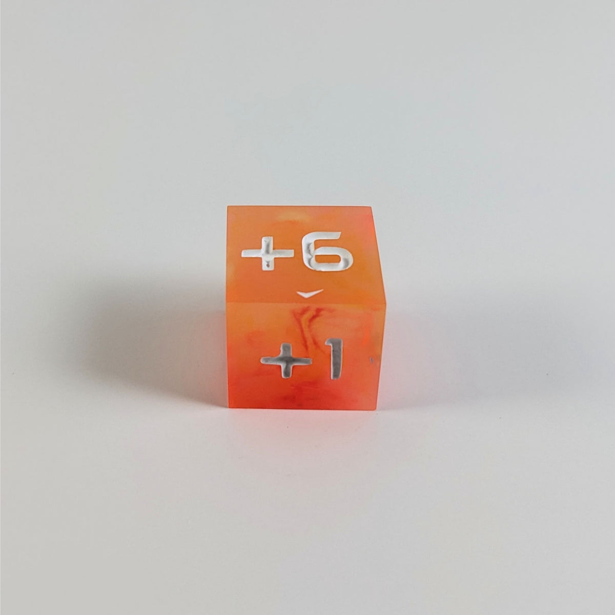 A low angle photo of an orange positive spindown d6 with white numbers sits on a white background with the +6 face up and the +1 face pointed towards the camera.