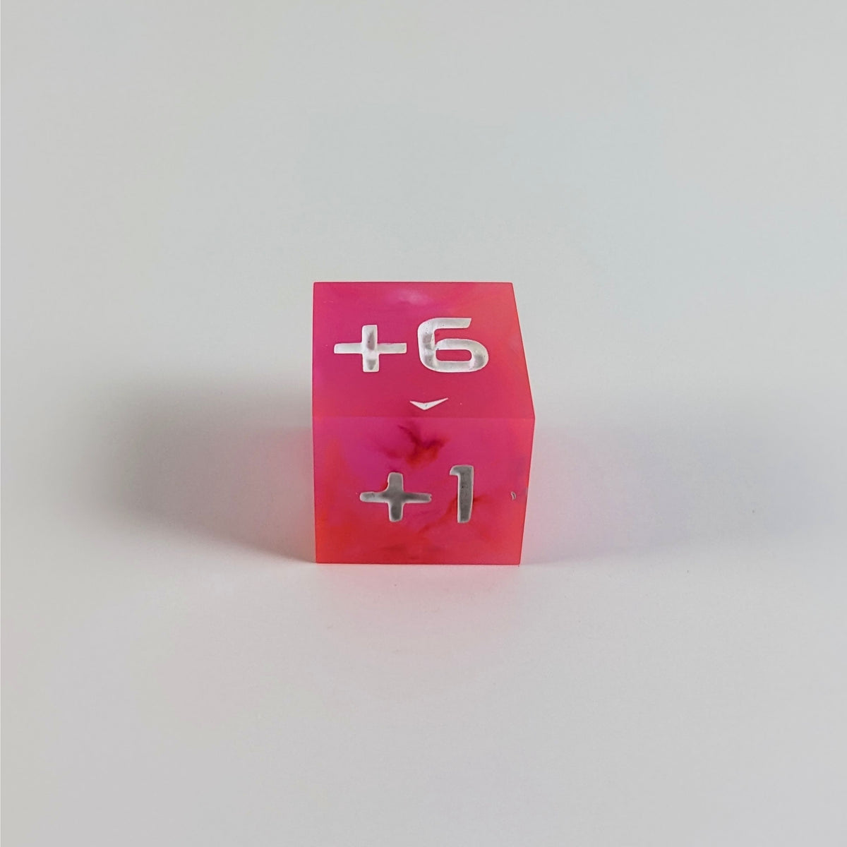 A low angle photo of a magenta positive spindown d6 with white numbers sits on a white background with the +6 face up and the +1 face pointed towards the camera.