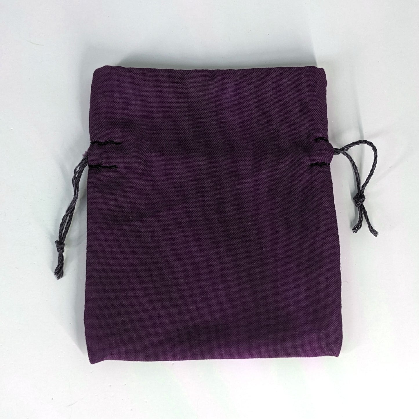 A small, handmade dice bag that is purple lays flat on a white background.
