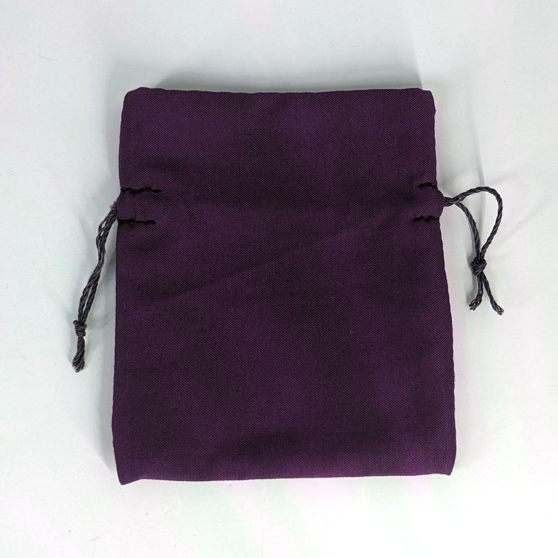 A small, handmade dice bag that is purple lays flat on a white background.