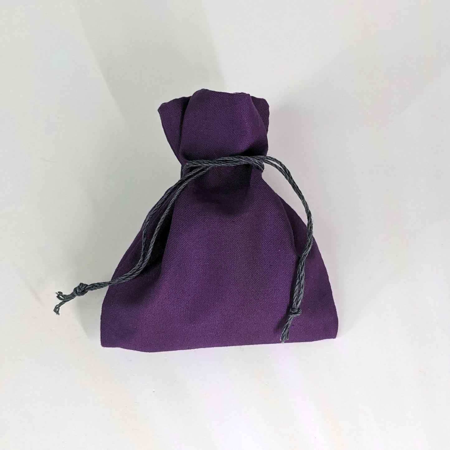 A small, handmade dice bag that is purple is tied closed on a white background.