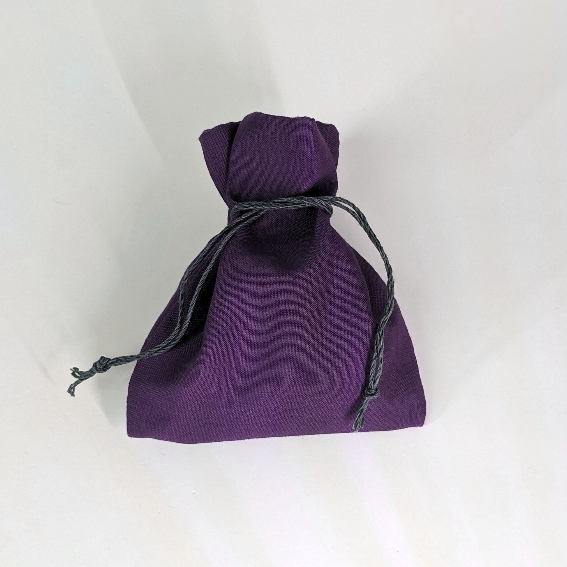 A small, handmade dice bag that is purple is tied closed on a white background.