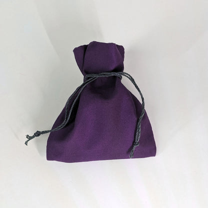 A small, handmade dice bag that is purple is tied closed on a white background.