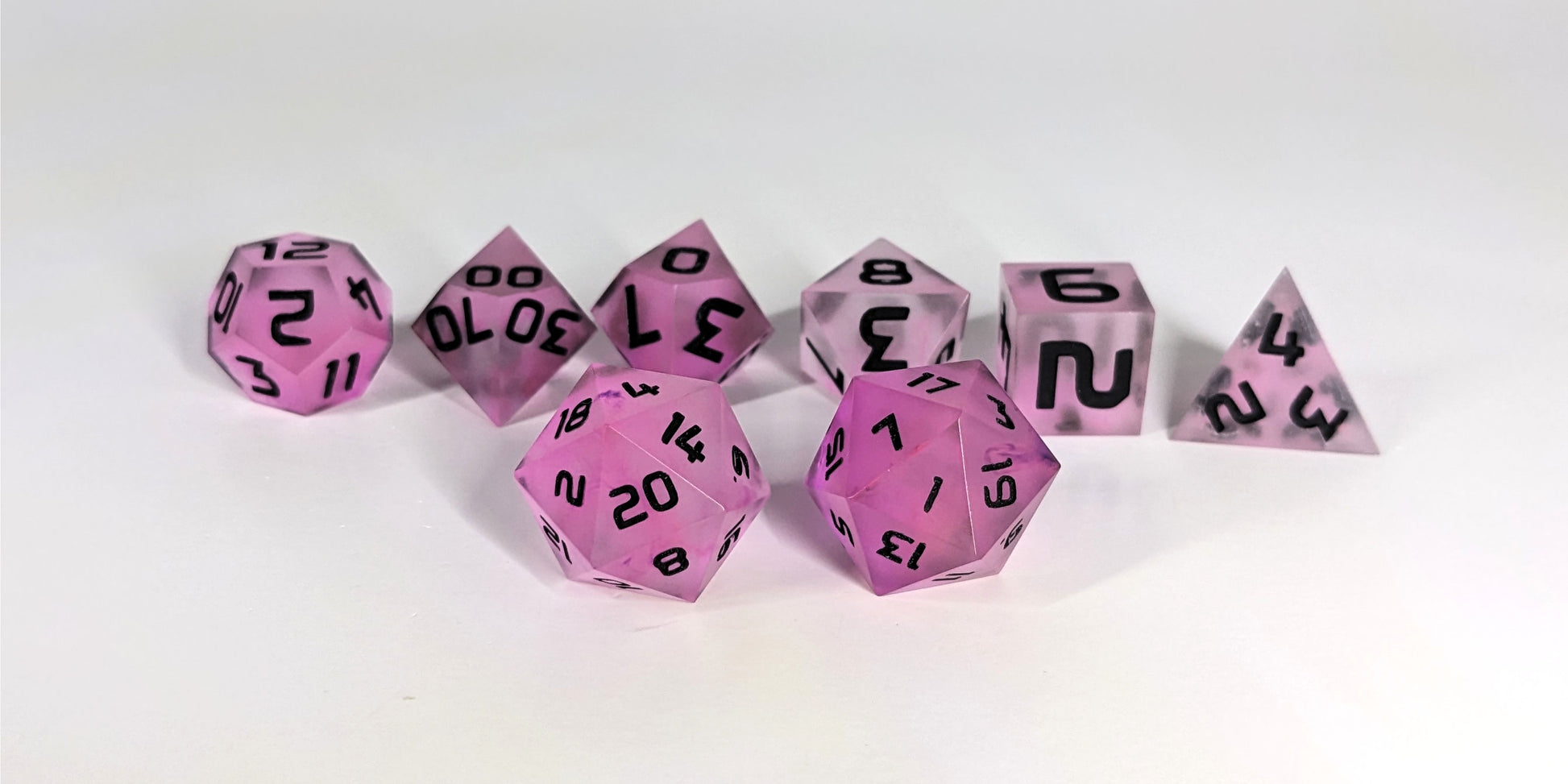 A straight on photo of a standard set of DnD dice that have pink/purple swirls and black numbers focusing on 2 d20s in the center. The d20 on the left has the 20 face centered and the d20 on the right has the 1 face centered. The other 6 dice are lined up in the background.