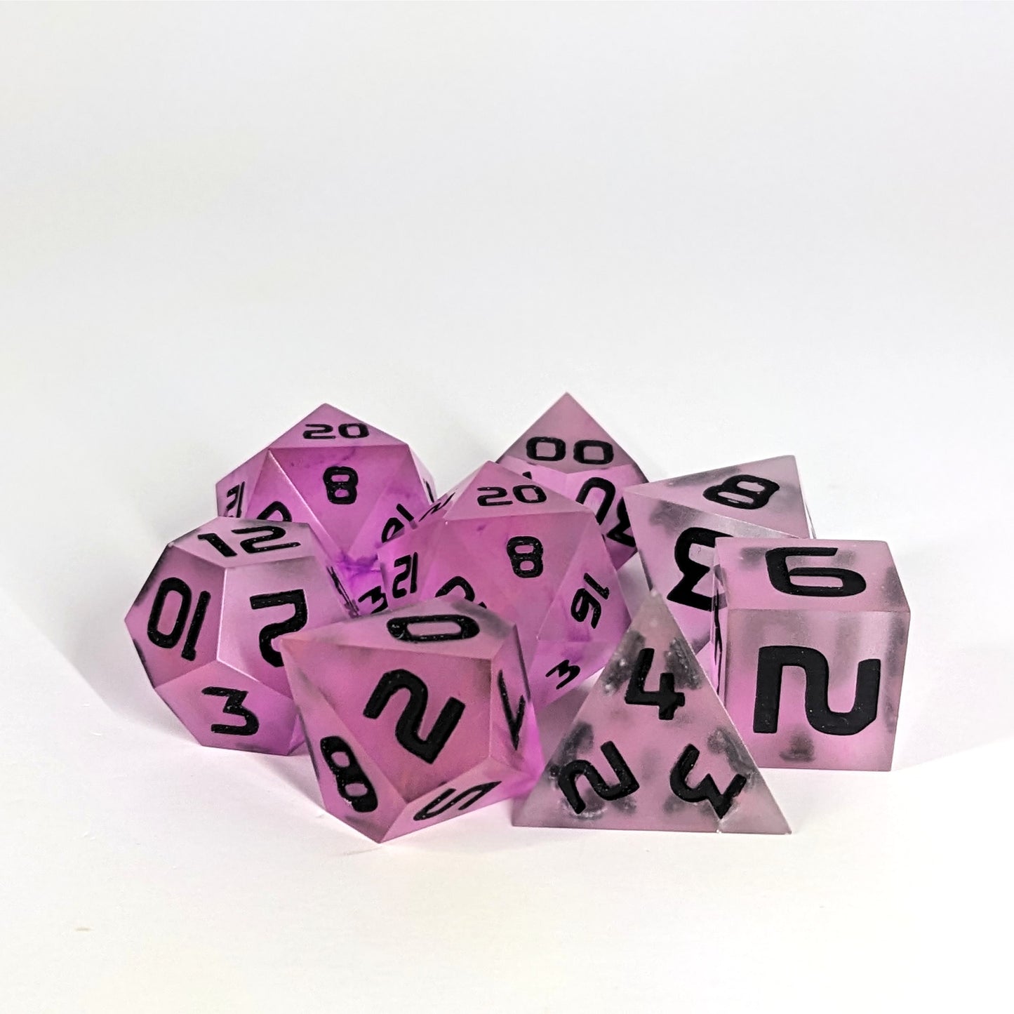 A complete set of 8 handmade artisan dice that have pink/purple swirls with black numbers. The DnD dice set is arranged in a circle and features 2 D20s, one of which is in the center surrounded by the other 7 dice.