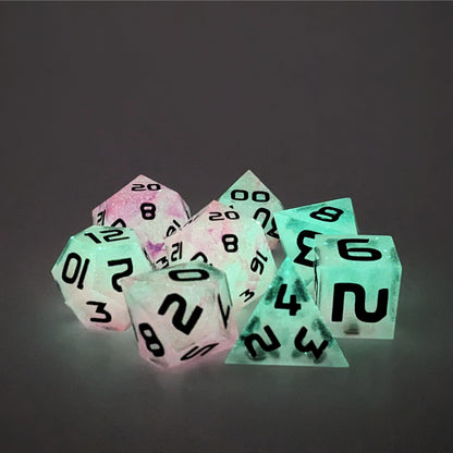 A complete set of 8 polyhedral dice that are glowing green with pink/purple swirls and black numbers, showing the glow-in-the-dark feature of this dice set. The DnD dice set is arranged in a circle and features 2 D20s, one of which is in the center surrounded by the other 7 dice.