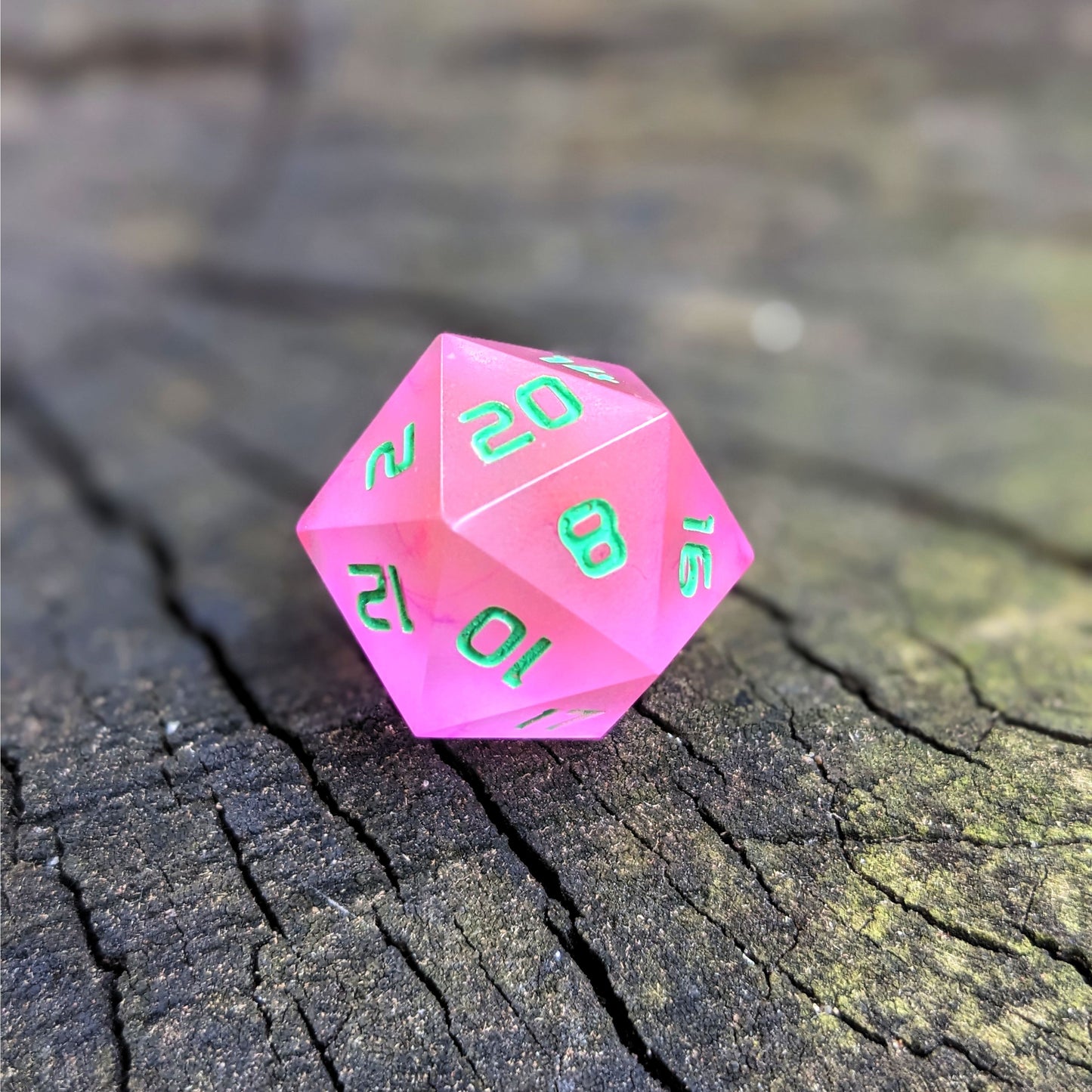 A standard d20 with pink/purple swirls and green numbers sits on a wood stump with the 20 face up.